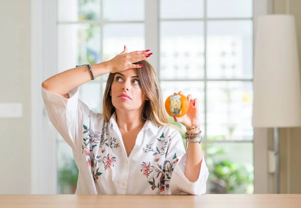 Ung Kvinna Hemma Hålla Ruttna Orange Stressad Med Handen Huvudet — Stockfoto