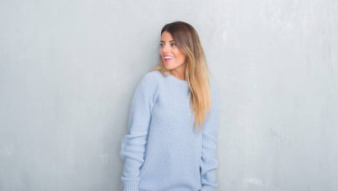 Gri grunge duvar kış kıyafeti uzak tarafına gülümseme ile yüzünde, doğal ifade arıyorum giyen genç yetişkin kadın. Kendine güvenen gülüyor.