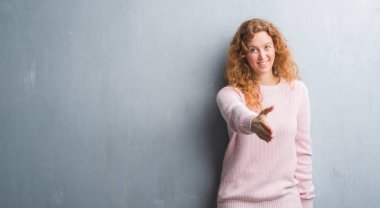 Genç redhead gri grunge duvar giyen üzerinde pembe kadın kazak tebrik ve konuksever dost sunan karşılıklı gülümseyerek. Başarılı iş.