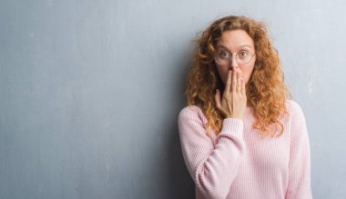 Gri grunge duvar gözlük kapak ağız elle hata, korku, sessizlik içinde gizli kavramı korkmuş ifade için utanç ile şok giyen genç Kızıl saçlı kadın