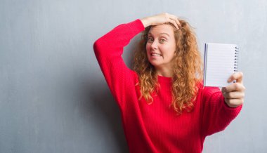 Genç Kızıl saçlı kadın boş dizüstü bilgisayar kafasına, el ile vurguladı gösterilen gri grunge duvarın üzerinden şok utanç ve sürpriz suratla, öfkeli ve sinirli. Korku ve hata için üzgün.