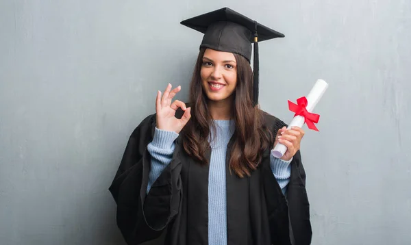 若いブルネットの女性グランジを灰色の優秀なシンボルの指で サインをして学位を保持壁着て大学院制服 — ストック写真