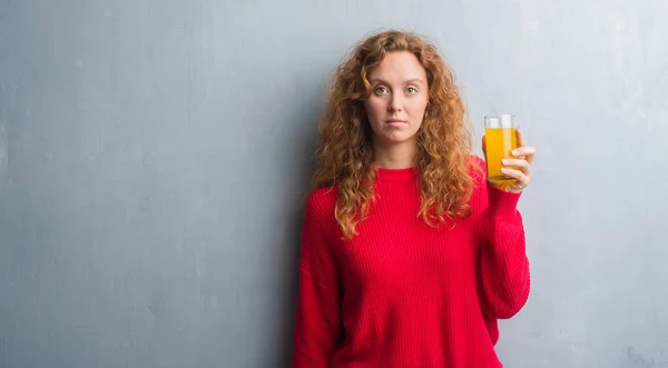 重大な考えるスマートの顔に自信を持って表現でのオレンジ ジュースのガラスを飲む灰色グランジ壁を越えて若い赤毛の女性 — ストック写真