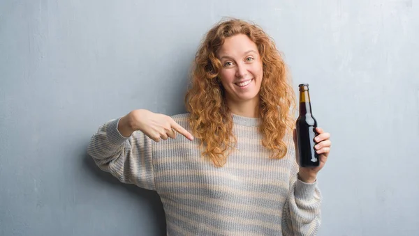 Joven Pelirroja Sobre Pared Grunge Gris Sosteniendo Botella Cerveza Con — Foto de Stock