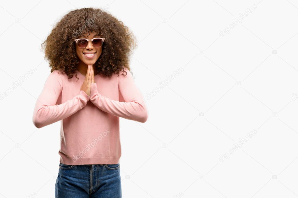 African american woman wearing pink sunglasses praying with hands together asking for forgiveness smiling confident.