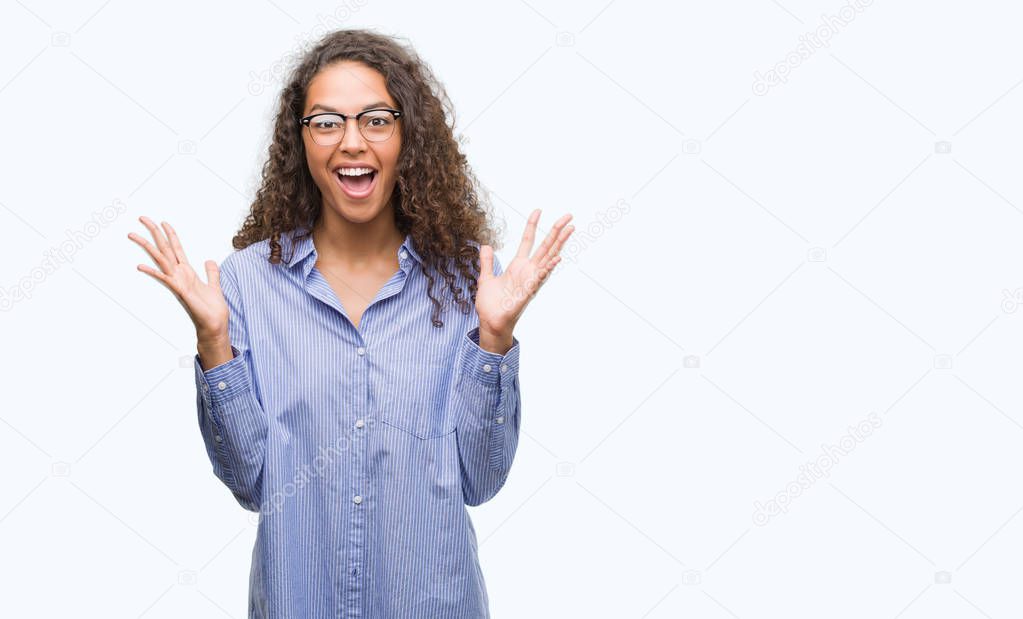 Beautiful young hispanic woman wearing glasses very happy and excited, winner expression celebrating victory screaming with big smile and raised hands