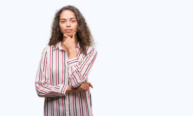 Güzel genç İspanyol kadın emin çapraz kollar ve çeneme kaldırdı el ile gülümseme ile kameraya bakıyor. Pozitif düşünce.