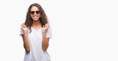 Genç İspanyol kadın geçiş parmakları umut ve gözleri kapalı ile gülümseyen güneş gözlüğü takıyor. Şans ve batıl kavramı.