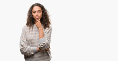 Emin çapraz kollar ve çeneme kaldırdı el ile gülümseme ile kameraya bakarak çizgili süveter giyen güzel genç İspanyol kadın. Pozitif düşünce.