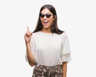 Genç güzel İspanyol bir fikir ya da soru işaret parmağı gülen yüz, bir numara ile sürpriz güneş gözlüğü takıyor