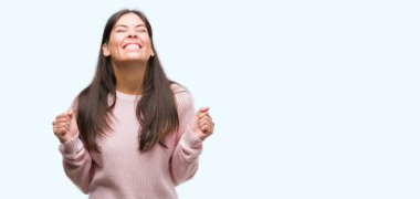 Silah ile başarı için heyecanlı bir kazak giyen genç güzel İspanyol kadın kutluyor zafer gülümseyen kaldırdı. Kazanan kavramı.