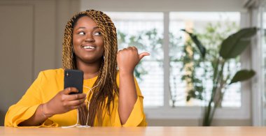 El ve parmak ile yukarı dönük mutlu yüz gülümseyen ile kulaklık ile akıllı telefon kullanan Afrikalı-Amerikalı kadın