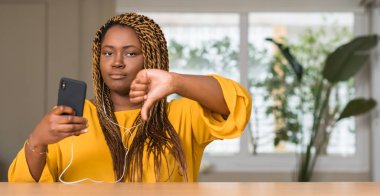 Kızgın yüz, eksi işareti aşağı antipati başparmak ile gösterilen, ret kavramı ile kulaklıklar ile akıllı telefon kullanan Afrikalı-Amerikalı kadın