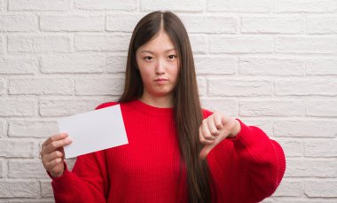 Kızgın yüz, eksi işareti aşağı antipati başparmak ile gösterilen, ret kavramı ile boş kağıt tutan tuğla duvarın üzerinden Genç Çinli kadın
