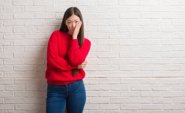 Tuğla duvar düşünme seyir üzerinde Genç Çinli kadın yorgun ve sıkılmış çapraz silah depresyon sorunları ile.