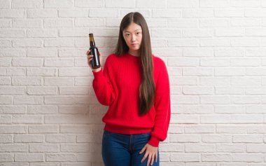 Genç Çinli kadın ciddi düşünme akıllı yüzünde kendinden emin bir ifade ile bira içme tuğla duvarın üzerinden