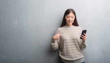 Kendisi için sürpriz yüz işaret parmağı ile smartphone vasıl seyir gri duvarın üzerinden Genç Çinli kadın