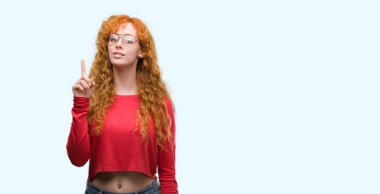 Bir fikir ya da soru işaret parmağı gülen yüz, bir numara ile sürpriz gözlüklü genç Kızıl saçlı kadın