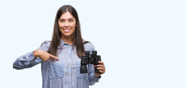 年轻的西班牙妇女手持双筒望远镜惊讶的脸指向自己的手指 — 图库照片
