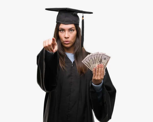 若いヒスパニック系女性を着て卒業制服持株ドルのカメラと指で指して 手に署名 正面からポジティブで自信のジェスチャー — ストック写真
