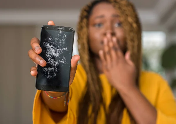 African american woman showing broken smartphone cover mouth with hand shocked with shame for mistake, expression of fear, scared in silence, secret concept