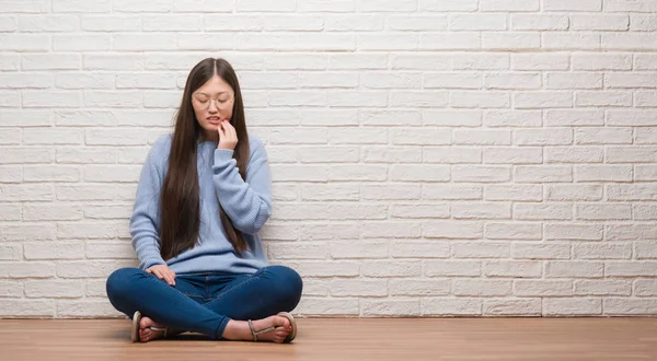 年轻的中国妇女坐在地板上 在砖墙上 手里带着痛苦的表情 因为牙痛或牙齿疾病 牙医概念 — 图库照片