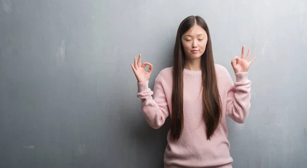 灰色の壁を越えて若い中国女性のリラックスし 瞑想の指ジェスチャーをやって閉じた目を浮かべてします ヨガの概念 — ストック写真