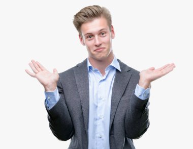 Genç yakışıklı sarışın iş adam clueless ve şaşkın bir ifadeyle kollar ve eller kaldırdı. Şüphe kavramı.