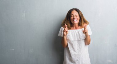 Umut ve gözleri kapalı geçiş parmaklarıyla gülümseyen gri grunge duvarın üzerinden duran orta yaş İspanyol kadın. Şans ve batıl kavramı.