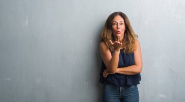 Bir öpücük el ile güzel ve seksi olmak hava üfleme kamera bakarak gri grunge duvarın üzerinden duran orta yaş İspanyol kadın. Aşk ifade.