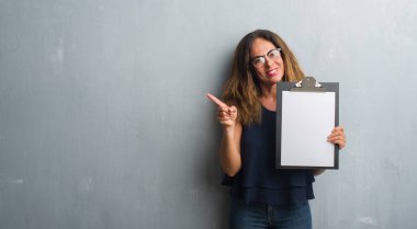 Gri grunge duvar holding Pano el ve parmak ile tarafına işaret çok mutlu üzerinde duran orta yaş İspanyol kadın