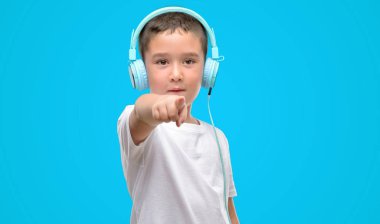 Koyu saçlı küçük çocuk kamera ve size parmak ile işaret kulaklık ile müzik dinleme, el işareti, pozitif ve kendinden emin bir jest ön