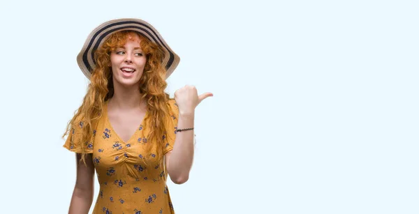 夏帽子と指していると幸せそうな顔を笑顔で側まで親指で示すのドレスを身に着けている若い赤毛の女性 — ストック写真
