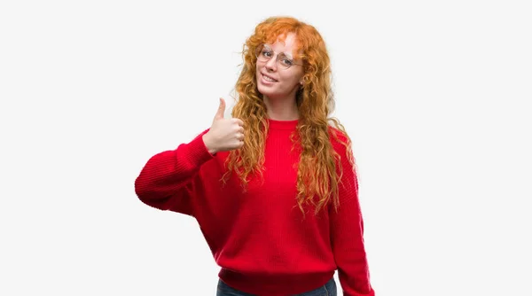 幸せの親指を手でジェスチャーをしている赤いセーターを着ている若い赤毛の女性 成功を示すと カメラを見て式を承認します — ストック写真