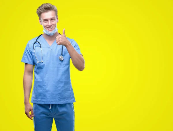若いハンサムな金髪医師の サイン 優秀な兆候を親指をやって大きな笑顔と幸せ — ストック写真