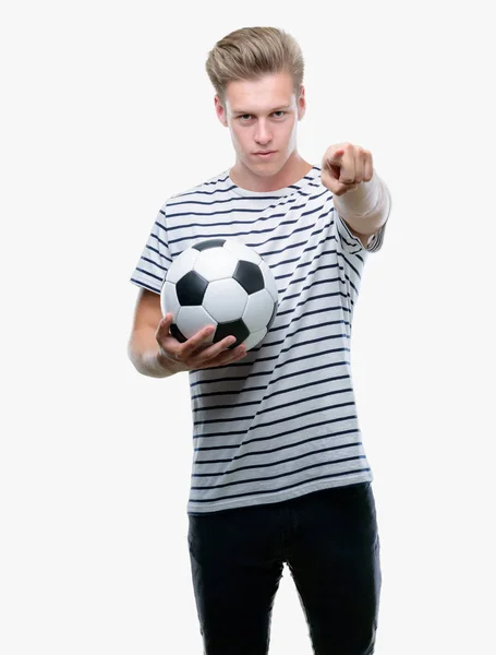 カメラと 正面からポジティブで自信のジェスチャーと指差し呼称サッカー ボールを保持している若いハンサムな金髪男 — ストック写真