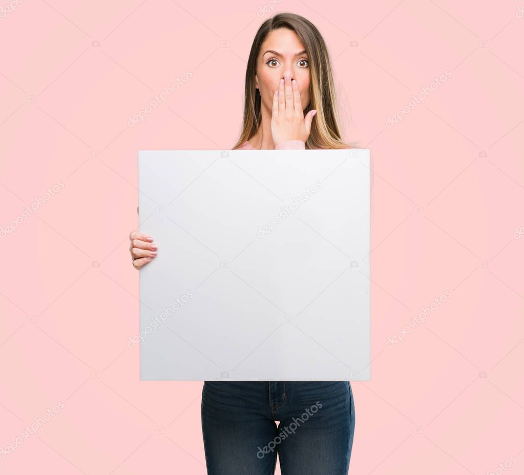 Beautiful young woman holding advertising banner cover mouth with hand shocked with shame for mistake, expression of fear, scared in silence, secret concept