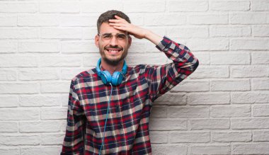 Genç yetişkin adam kafasına, el ile vurguladı kulaklıklar giyen tuğla duvarın üzerinden şok utanç ve sürpriz suratla, öfkeli ve sinirli. Korku ve hata için üzgün.