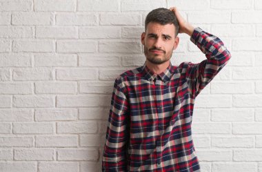 Genç yetişkin adam beyaz tuğla duvarı ayakta yanıltır ve soru hakkında merak ediyorum. Şüphe, kafasına el ile düşünme ile belirsiz. Dalgın kavramı.