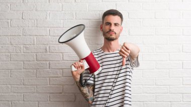 Başparmak aşağı, ret kavramı ile eksi işareti gösteren genç yetişkin adam holding megafon kızgın yüzü ile sevmemek