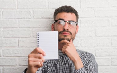 Beyaz tuğla duvar ciddi bir yüz düşünme hakkında soru, çok karışık bir fikir üzerinde dizüstü ayakta tutan genç yetişkin adam