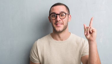 Gri grunge duvar bir fikir ya da soru işaret parmağı ile gülen yüz, sürpriz genç beyaz adam bir numara