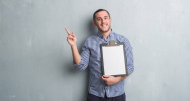 Pano çok mutlu el ve parmak ile tarafına işaret tutan gri grunge duvarın üzerinden beyaz delikanlı