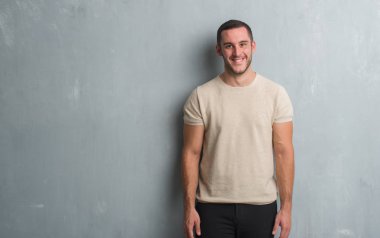 Beyaz delikanlı gri grunge duvarın yüzünde mutlu ve güzel bir gülümseme ile üzerinden. Şanslı kişi.