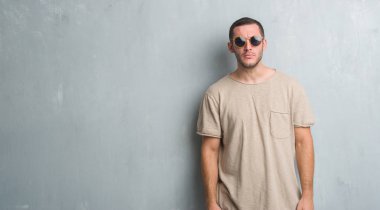 Beyaz genç güneş gözlüğü şüpheci ve sinir, papatyanın üzgün sorunu nedeniyle giyen gri grunge duvarın üzerinden. Negatif kişi.