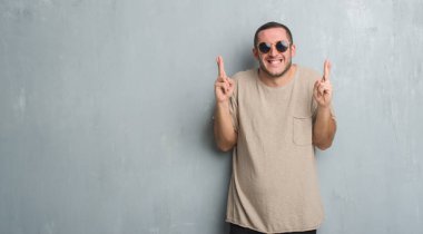 Beyaz delikanlı geçiş parmakları umut ve gözleri kapalı ile gülümseyen güneş gözlüğü takıyor gri grunge duvarın üzerinden. Şans ve batıl kavramı.