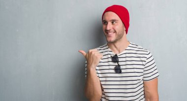 İşaret ve başparmak kadar mutlu yüz gülümseyen tarafı ile gösterilen yün şapkası gri grunge duvarın üzerinden beyaz delikanlı