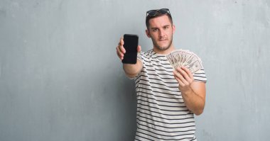 Dolar ve smarphone tutan gri grunge duvarın üzerinden beyaz delikanlı 