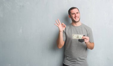 Bir parmak, mükemmel sembolü ile ok işareti yapıyor dolar gösterilen gri grunge duvarın üzerinden beyaz delikanlı