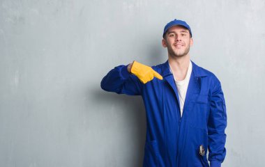 Sürpriz yüz işaret parmağı kendine mekanik üniforması gri grunge duvarın üzerinden beyaz delikanlı